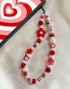 a red and white beaded necklace next to a cell phone with hearts on it