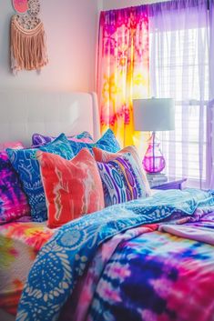 a bed with colorful comforters and pillows in front of a window filled with curtains