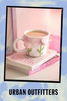 a cup of coffee sitting on top of a book next to a pink flowered wall