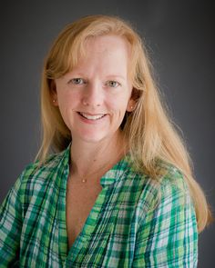 a woman with blonde hair wearing a green and white checkered shirt smiling at the camera