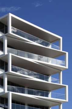 a tall white building with balconies against a blue sky and clouds in the background