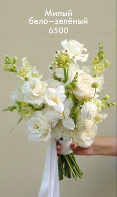 a bouquet of white flowers is held by a woman's hand in front of a wall