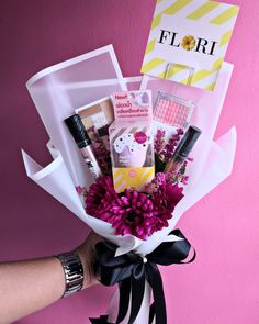 a person holding a bouquet of flowers and personal items in front of a pink wall