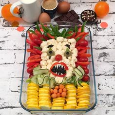 a platter filled with vegetables and fruit in the shape of a clown's face