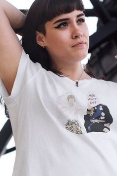 a woman in white shirt holding her hand up to her head and looking at the camera