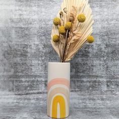 a vase filled with dried flowers on top of a gray surface and a wall behind it