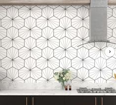 a kitchen with black cabinets and white tiled backsplashes, an oven hood over the stove