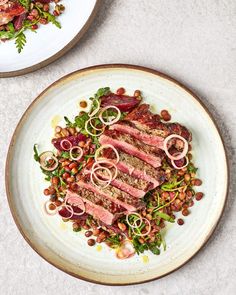 a white plate topped with meat and veggies next to another plate filled with food