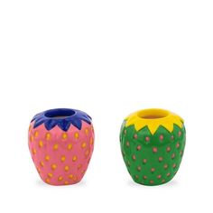 two colorful vases sitting next to each other on a white surface, one has a strawberry and the other has a blue top