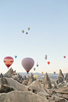 many hot air balloons are flying in the sky above some rocks and boulders on a sunny day