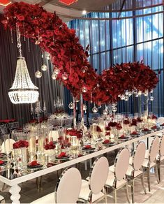 a long table is set with white chairs and red flowers on the centerpieces