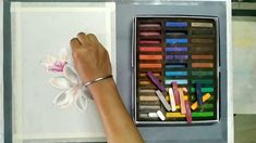 a woman's hand next to a box of crayons and colored pencils