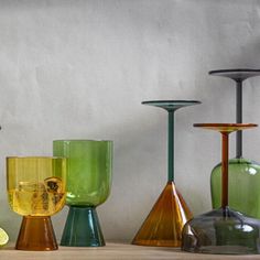 several different colored glass vases on a table next to each other with one yellow piece in the middle