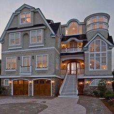 a large gray house with lots of windows and lights on the front door is lit up at night