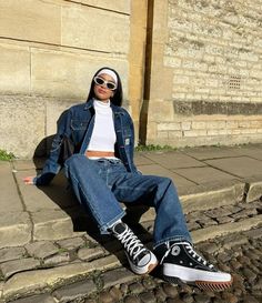 a woman sitting on the steps with her legs crossed wearing jeans and white shirt, black converse sneakers