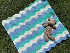 a crocheted teddy bear is laying on a blue and white blanket in the grass