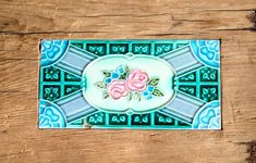 a blue and green tile with pink flowers on the bottom is sitting on a wooden surface