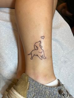 a small tattoo on the ankle of a woman's leg with a dog holding a heart