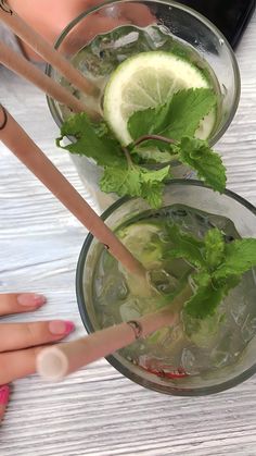 two glasses filled with ice and limes on top of a white table next to each other