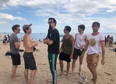 four men standing on the beach talking to each other and one man holding a frisbee