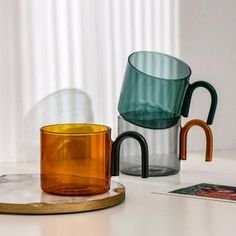 three different colored glass cups sitting on top of a white table next to each other