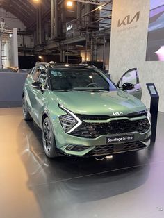 a green suv is on display in a showroom with two other vehicles behind it