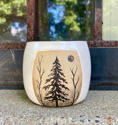 a white bowl with trees painted on the side sitting on top of a counter next to a window