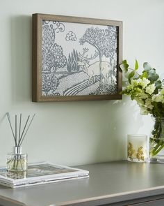 a vase with flowers and reeds sitting on top of a table next to a painting