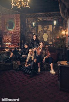 four women sitting on a couch in a dark room with a chandelier hanging from the ceiling