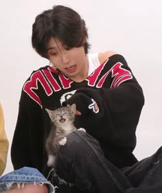 a person sitting on the ground with a cat in their lap and one hand holding a kitten