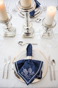 a table set with silverware, candles and napkins