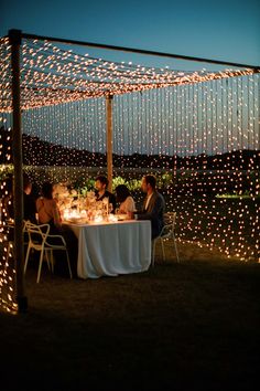 people are sitting at a table under string lights