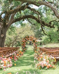 an outdoor ceremony setup with wooden chairs and floral arrangements on the aisle, surrounded by trees