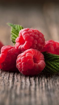 raspberries with green leaves on wooden surface