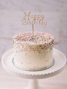 a white cake with sprinkles and a happy birthday sign on top