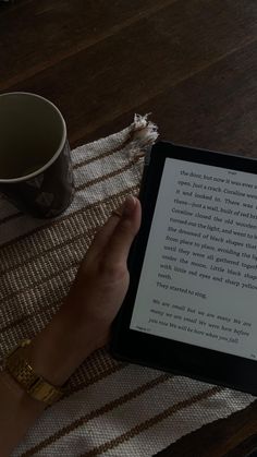 a person holding an electronic device on top of a table next to a cup of coffee