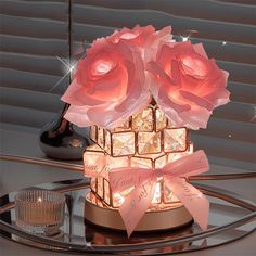 pink roses are lit up on top of a small box with lights in the shape of cubes