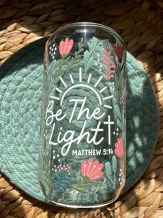 a glass jar with the words be the light on it sitting on a woven place mat