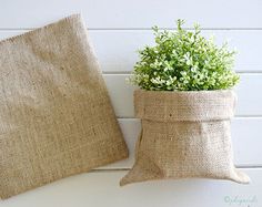 a plant in a burlap sack next to a pillow on a white wall