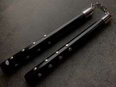 two black pool cues with silver studded ends on a dark surface, one has a key chain attached to it