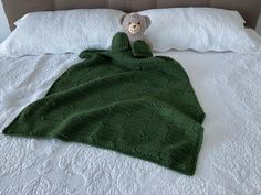 a teddy bear wrapped in a green blanket on top of a bed with white sheets