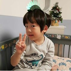 a little boy sitting on top of a bed giving the peace sign