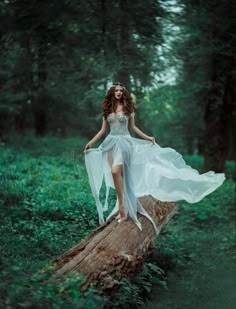 a beautiful young woman in white dress walking on a log in the woods stock photo