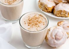 two glasses filled with cinnamon rolls next to some doughnuts on a white table