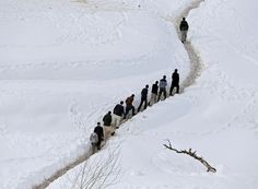 a long line of people walking up a snow covered hill in the winter, with no one on it