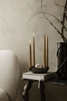 four candles are sitting on top of a book next to a vase with branches in it