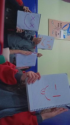 several children holding up notebooks with drawings on them and writing numbers in the middle