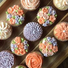 cupcakes with frosting and flowers are arranged on a wooden tray