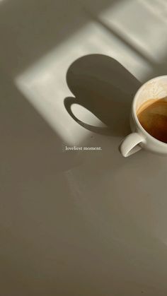 a cup of coffee sitting on top of a white table next to a shadow from the window