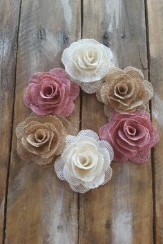 three different colored flowers are placed on a wooden table with burlocked fabric